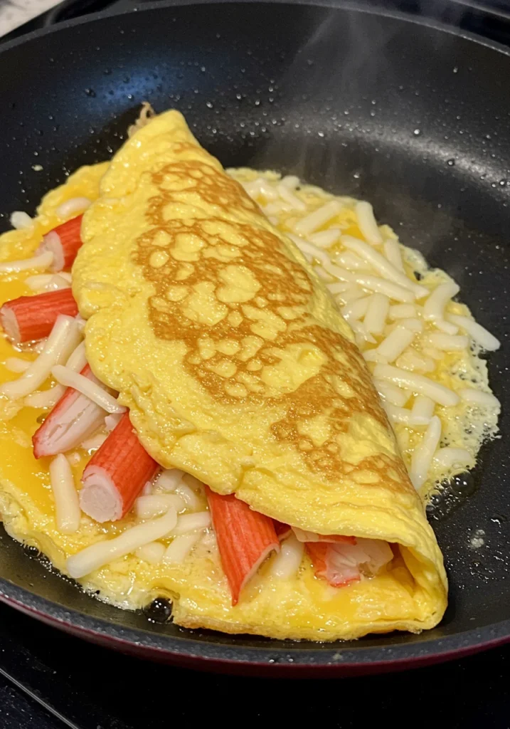 Progress photo of a crab meat omelette being cooked in a skillet with visible crab and melted cheese.